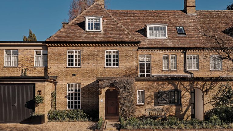 De la Californie à Cambridge – comment cette famille a trouvé une nouvelle vie dans une vieille maison anglaise qui fusionne la tradition avec un style de côte ouest décontracté Front view of a traditional brick townhouse with white-framed windows, pitched tile roof, and a wooden front door surrounded by creeping vines