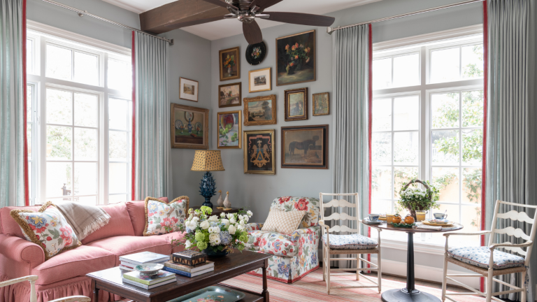 Je pensais que j’étais sur les murs de la galerie, mais cette méthode de suspension approuvée par des concepteurs a changé d’avis – cela rend les coins maladroits « plus doux, en couches et vécus » a traditional living room with a large pink couch, a coffee table with books and a vase of flowers, a floral accent chair, and a cluster of art hung in the corner of the room