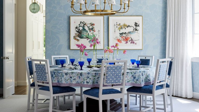 Cette propriétaire voulait retourner dans la maison qu’elle a construite il y a plus de 20 ans – elle a donc donné à un designer totalement libre de changer pour changer absolument tout Dining room with floral blue wallpaper and a circular dining table. Blue and white chairs sit around the table and a gold chandelier hangs above