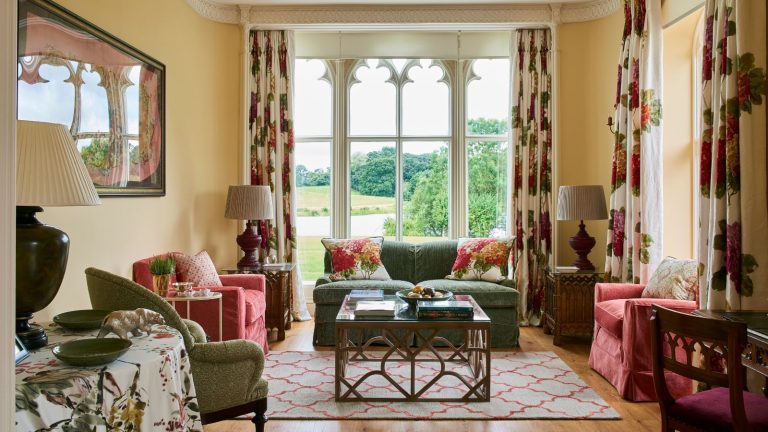 « C’est la différence entre une pièce qui se sent lancée ensemble et celle qui coule ‘- les concepteurs expliquent la règle des 4 sièges 4 et pourquoi vous devriez le suivre Living room with wooden floor and gothic window with views to the garden. Red and green upholstered chairs and sofa and floral curtains and cushions.
