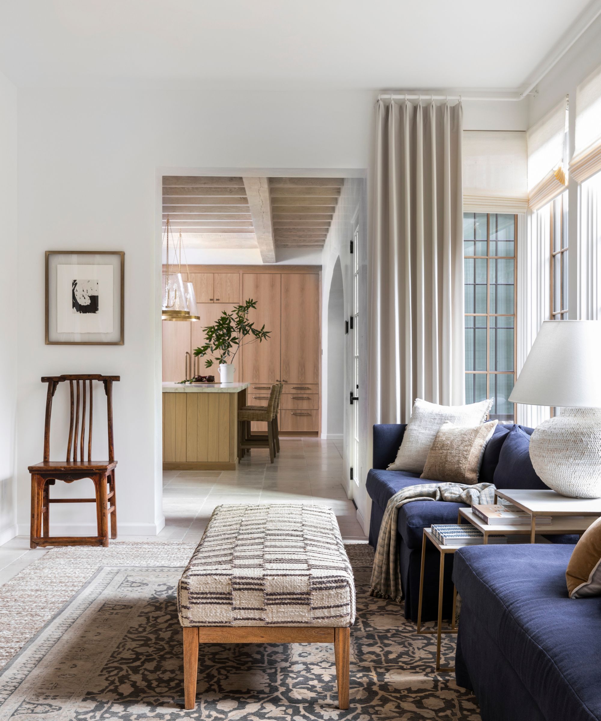 Véranda avec des murs blancs et de grandes fenêtres, avec un canapé bleu et un tapis à motifs et un banc