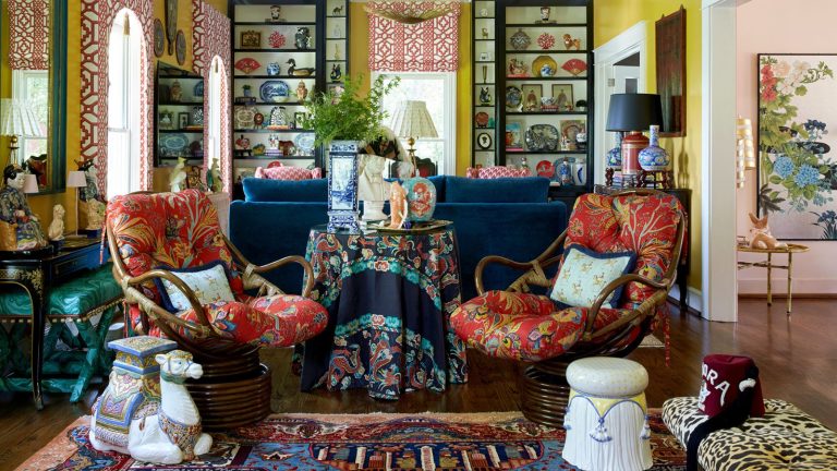 Cette fois l’année dernière maximalist living room with yellow walls, bookcases filled with antiques, large blue couch, red upholstered antique chairs, ceramic stool and leopard bench