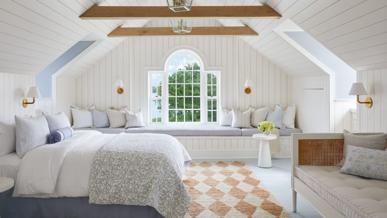 « C’est là que la tradition patrimoniale rencontre la facilité de vie pieds nus près de l’eau » – c’est comment clouer l’esthétique de «Eastcoastal», selon un designer qui le vit toute l’année Eastcoastal bedroom featuring a cream-and-white diamond pattern jute area rug, patterned bedding, a high thatched ceiling with exposed wood planks, and a window daybed on the far side of the room