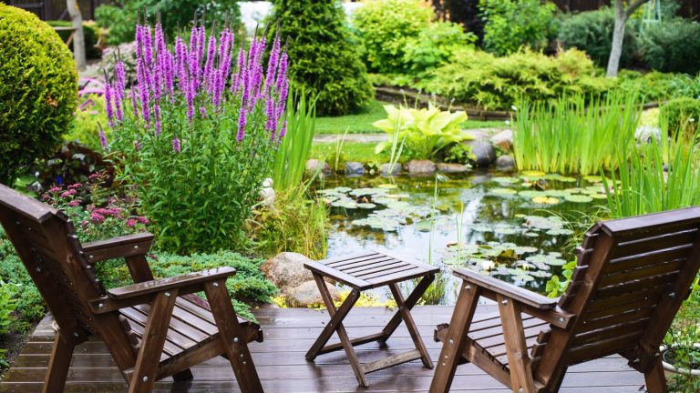 J’ai conçu et géré des jardins thérapeutiques tout au long de ma carrière, et je connais les 7 éléments essentiels de la création d’un jardin de bien-être réparateur Two wooden chairs and a table next to a pond