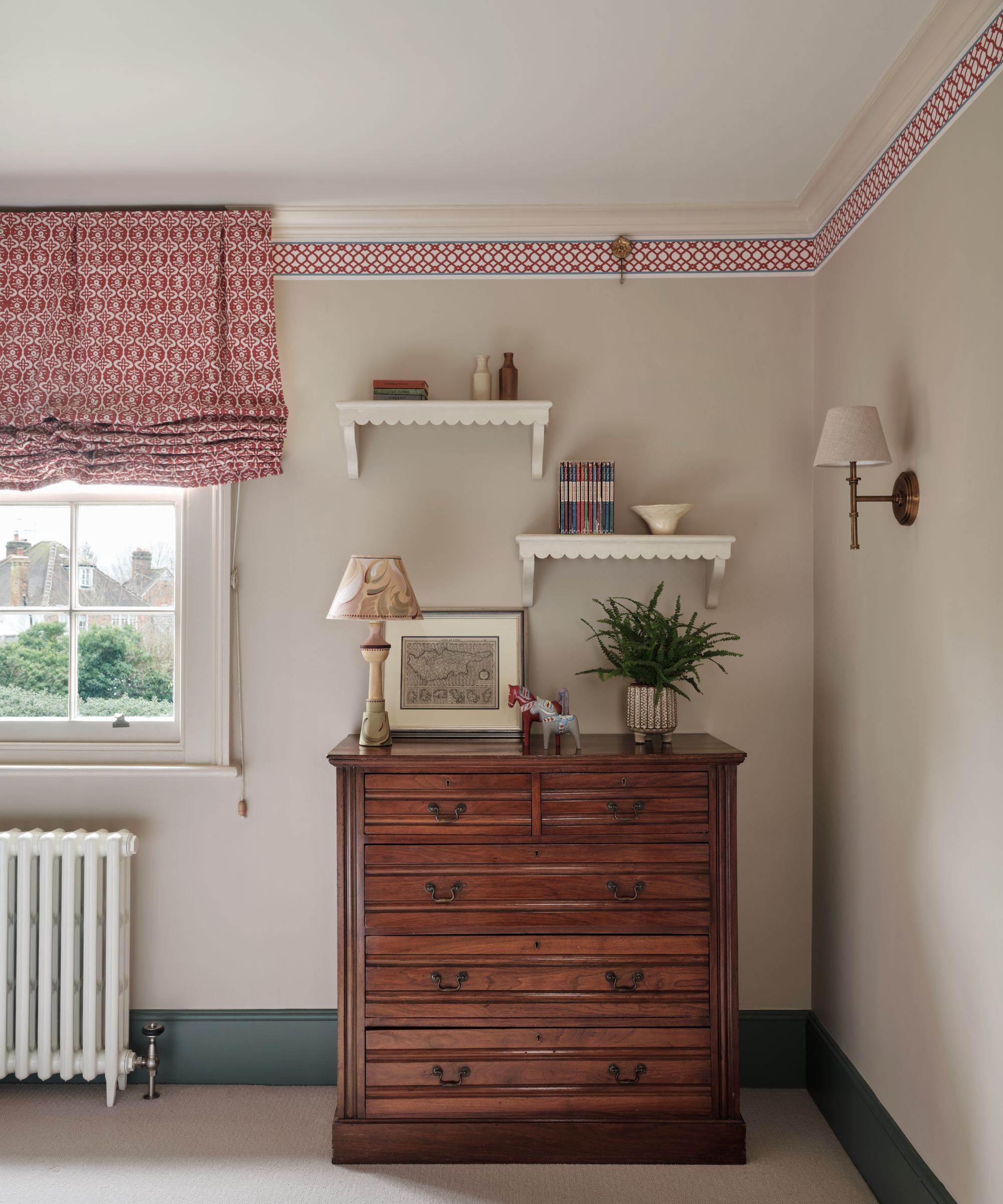 Chambre à coucher avec murs gris pâle, garniture de plafond et stores rouges assortis, coffre en bois antique de tiroirs et d'applications