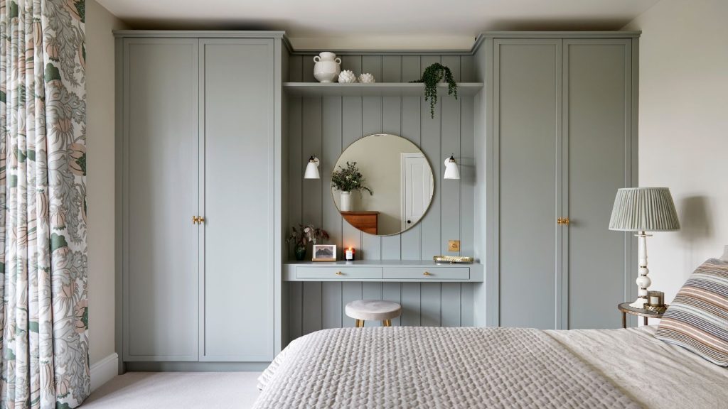 Bedroom with grey painted built-in cabinetry and vanity unit, cream carpet, and double bed with quilted throw