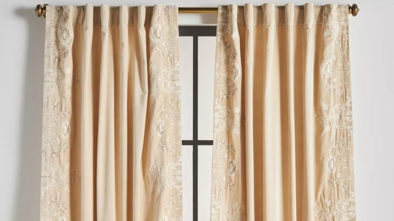 Comment les rideaux en velours les plus vendus d’Anthropologie ont transformé l’espace de stockage dans mon petit appartement Anthropologie Harlowe curtain panels in Ivory hanging from a decorative brass curtain rod over a tall windowpane.