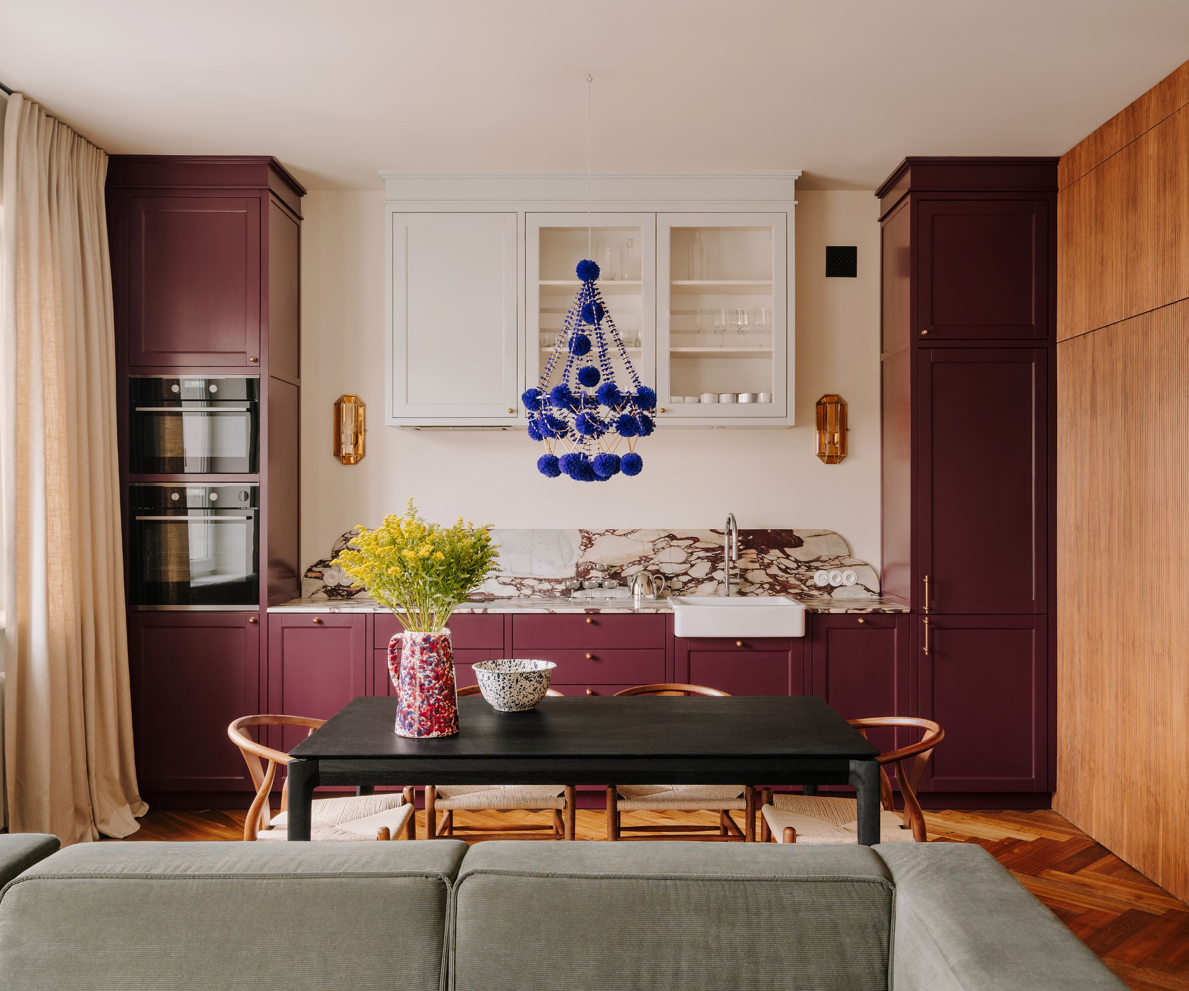 Cuisine à plan ouvert avec armoires peintes aubergins, comptoirs en marbre, armoires blanches et table à manger avec chaises en bois