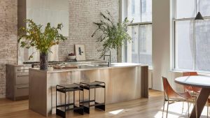 Toutes les cuisines les plus élégantes que je vois en ce moment ont des comptoirs en acier inoxydable – mais sont-ils un bon choix ainsi qu’un bon choix? An open plan stainless steel kitchen with an island and vases filled with seasonal greenery