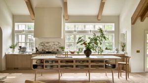 A Coastal Scandinavian kitchen with wooden cabinetry, warm white walls, and high ceilings