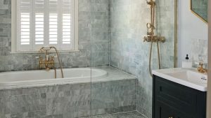 Au revoir les baignoires blanches ennuyeuses, toutes les salles de bains les plus chics que je vois en ce moment présentent ce design de carreaux inattendu à la place A gray bathroom with a tiled bath and a gold shower faucet