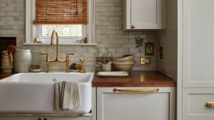 A neutral kitchen with gray cabinets, a tiled wall, wooden countertops, and a brass faucet