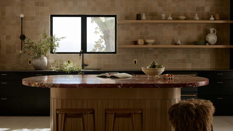 Les comptoirs en marbre bordeaux sont devenus ma tendance préférée de 2025 – et les designers conviennent que c’est le matériau parfait pour une cuisine plus unique A warm neutral kitchen with tiled walls, black cabinetry, and a curved wooden island topped with a burgundy marble countertop