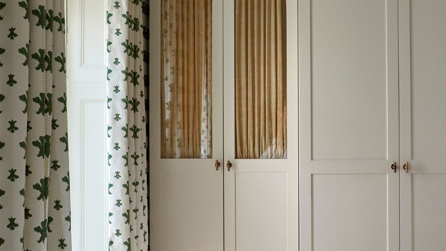 Agrandissez discrètement votre placard compact avec un rail pliable Joseph Joseph à 17 $, rapide à installer et caché à la vue de tous. neutral wardrobes with glass front closet door with a cabinet curtain behind and brass hardware