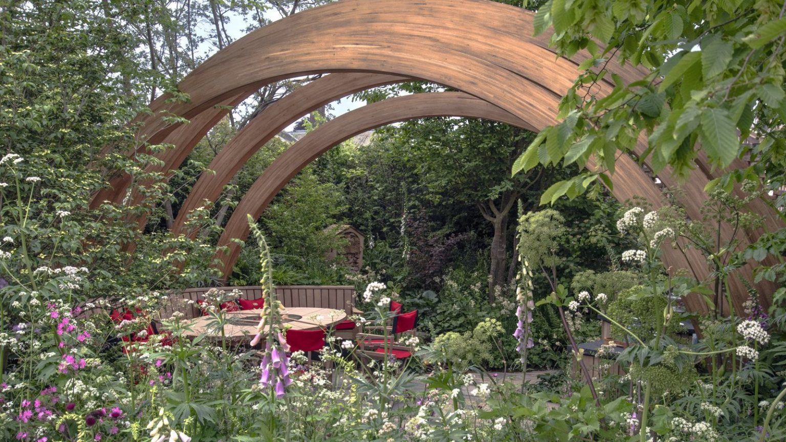 5 tendances inspirantes en matière d’aménagement paysager qui définiront 2026 – et pourquoi les concepteurs disent qu’ils sont là pour rester A show garden at Chelsea Flower Show with trees, shrubs, and flowering perennials under a large wooden arch