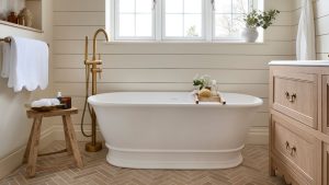 paneled cream bathroom with a light oak scalloped vanity, white freestanding bath with a wooden stool