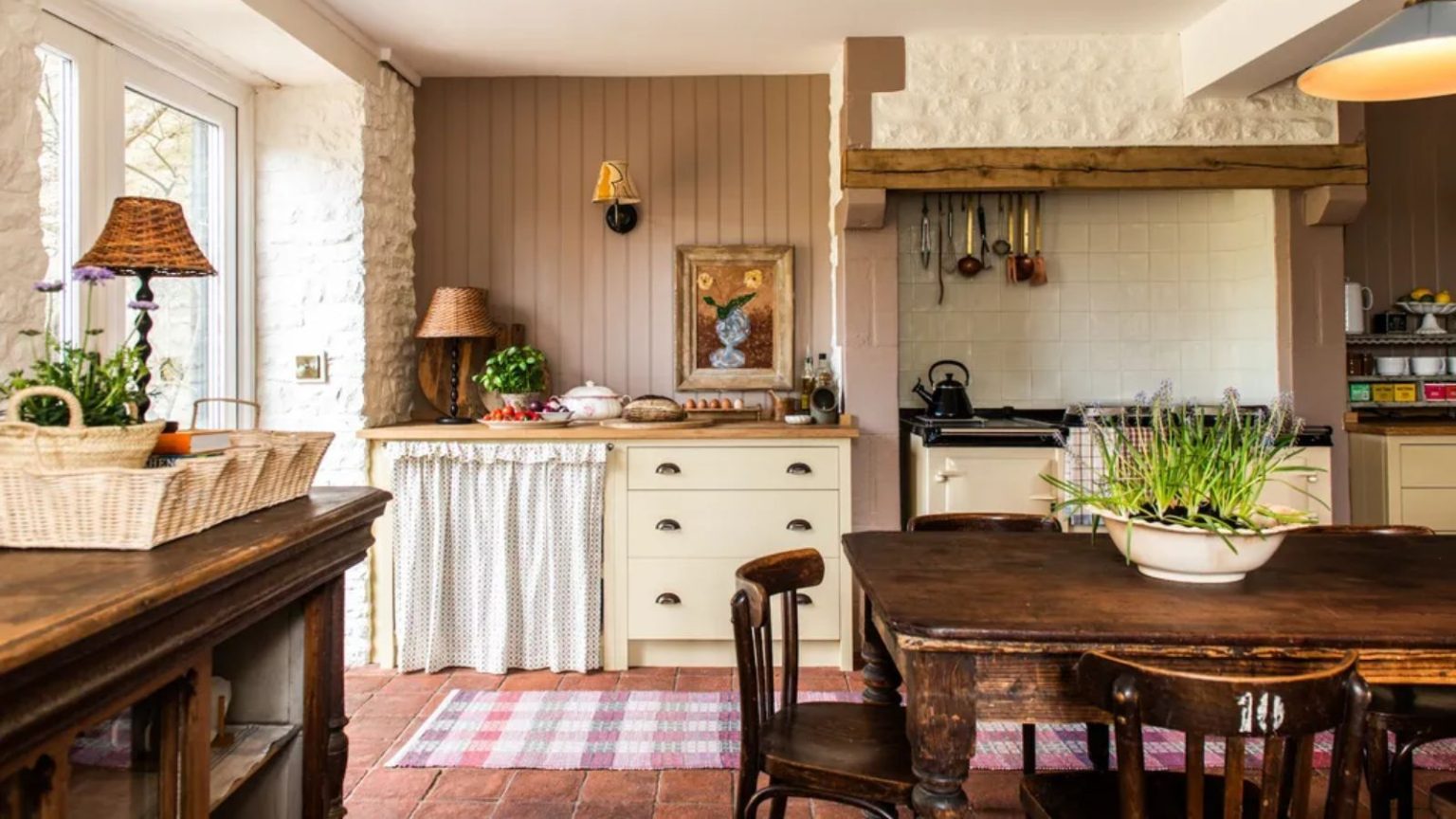 J’ai demandé aux designers leurs meilleurs conseils pour rendre une cuisine plus accueillante et magique pour Thanksgiving – voici ce qu’ils ont dit country vintage english kitchen with cream cabinet, dark pink paneled walls, rustic vintage wooden table and chairs