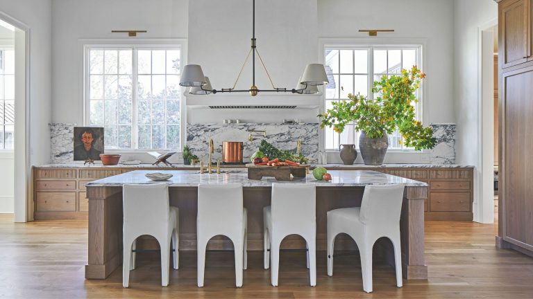 Une histoire de deux styles : l’élégance française rencontre la fraîcheur de Nashville dans cette maison du sud à l’âme européenne A large airy kitchen with white walls and wooden cabinets. The is a large kitchen island in the center with white chairs and a pendant light hanging above