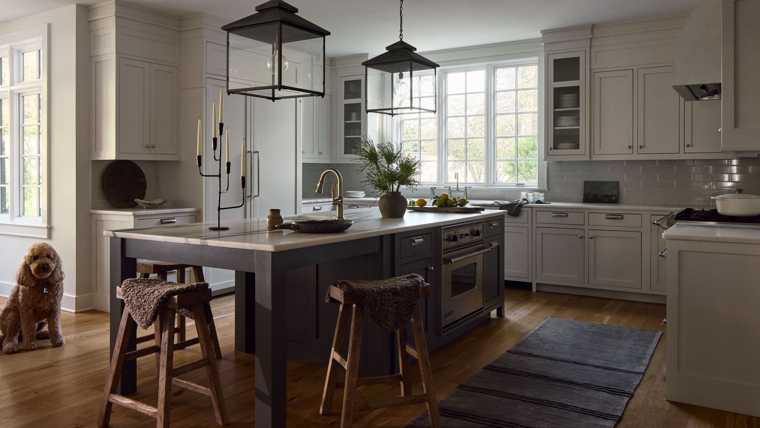 Grande cuisine avec armoires murales gris pâle et un îlot gris foncé au centre. Deux suspensions lanternes sont suspendues au-dessus et des outils en bois rustiques permettent de s'asseoir à une extrémité.
