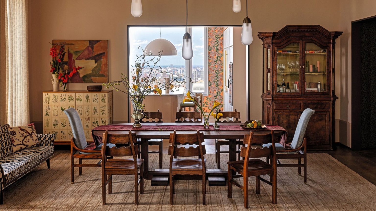 Comment la designer Heide Hendricks a apporté du caractère, de la couleur et de l’histoire à un penthouse moderne et terne de Manhattan Dining room with creamy plaster pink wallas and a large wooden dining table and vintage wooden chairs in the middle. An antique glass fronted cabinet is in one corner and a vintage sofa under the window