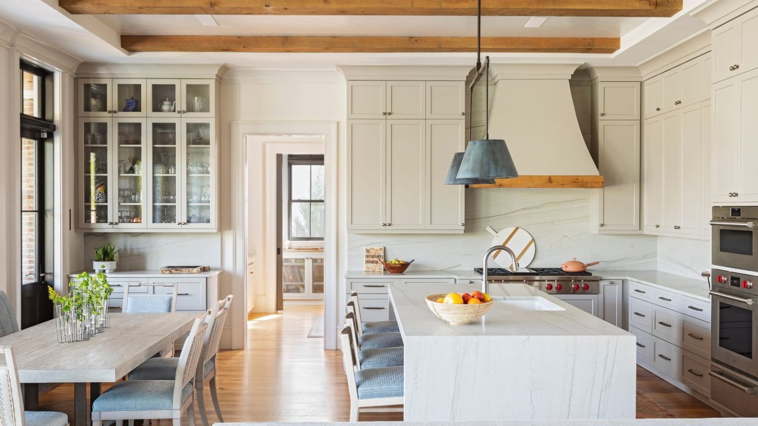 5 caractéristiques de cuisine personnalisées que les concepteurs pensent que vous devriez prendre en compte si vous rénovez en 2026 A large neutral kitchen with custom cabinets and range hood, a large island, and a small dining space