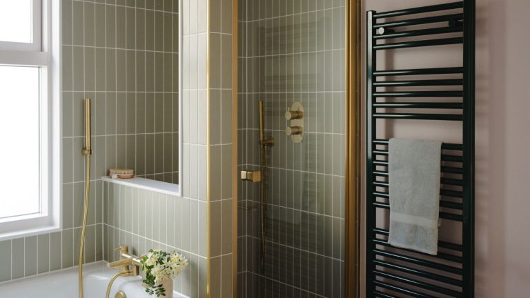 Je n’ai pas d’espace dans mon petit rangement de salle de bain pour les serviettes, mais ces joyaux pliables à 7 $ sont la solution parfaite A bathroom with a green-tiled freestanding shower, beside a bathtub. A black wall mounted towel radiator beside the glass shower door.