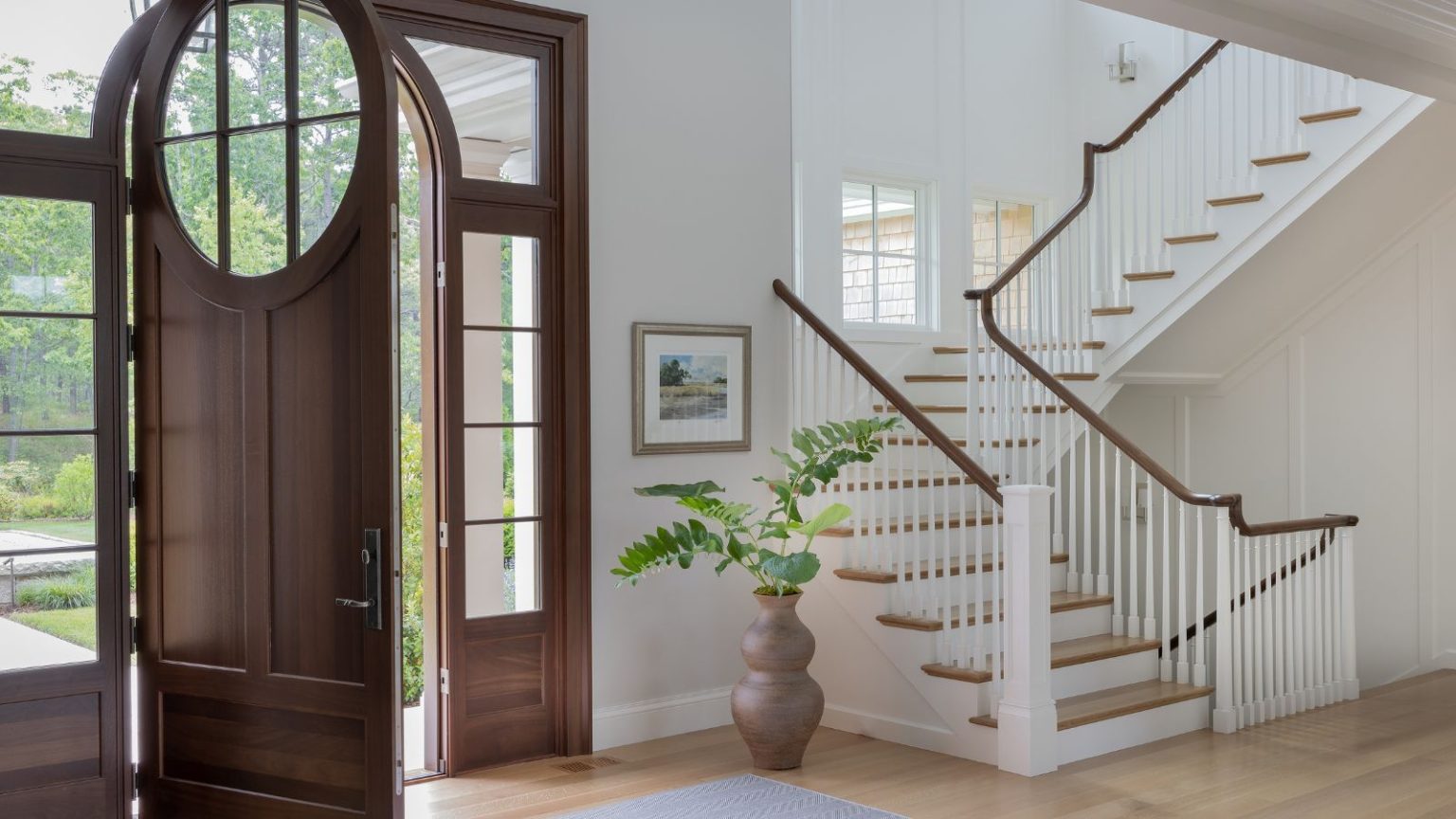 Enfin! Un bac à bottes chic qui élimine pour toujours les empreintes boueuses et mouillées – avec style Large white, bright entryway with open wooden door and winding stair case showing step up to first floor, and down to basement level. It all features extensing hardwood flooring