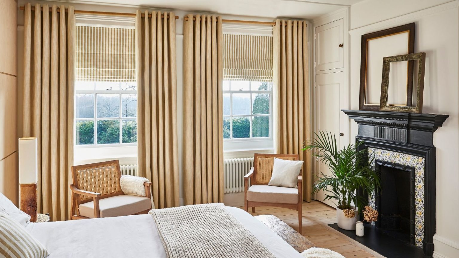La première grosse erreur de gel que tout le monde fait avec Windows – et le projet de correctif sophistiqué à 54 $ que les concepteurs adorent A neutral bedroom with beige curtains and blinds. Two rattan arm chairs face the bed, and a black fireplace opposite.
