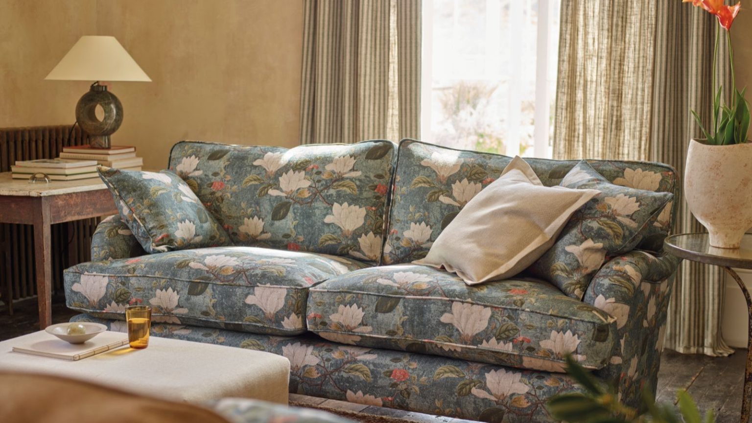 « Ce sont des micro-environnements dans lesquels la moisissure se développe » – Les experts exhortent les propriétaires à désencombrer 5 choses dès maintenant pour éviter l’humidité cet hiver Cozy living room with blue sofa that has a large floral pattern, and floor length linen curtains letting in light where thick lined ones would not