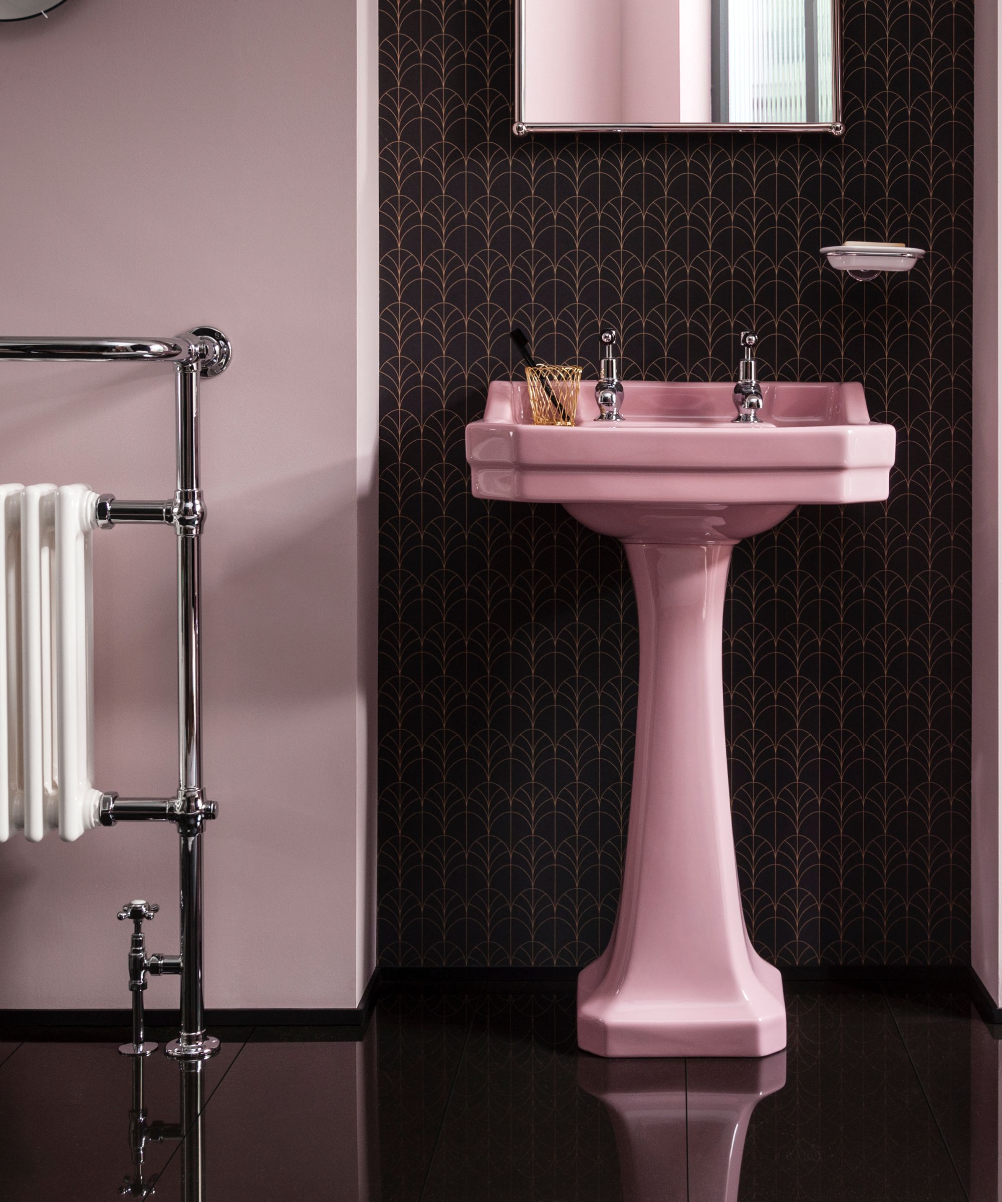 Une salle de bains rose et chrome avec du papier peint noir et doré, un miroir et un radiateur avec des carreaux noirs brillants