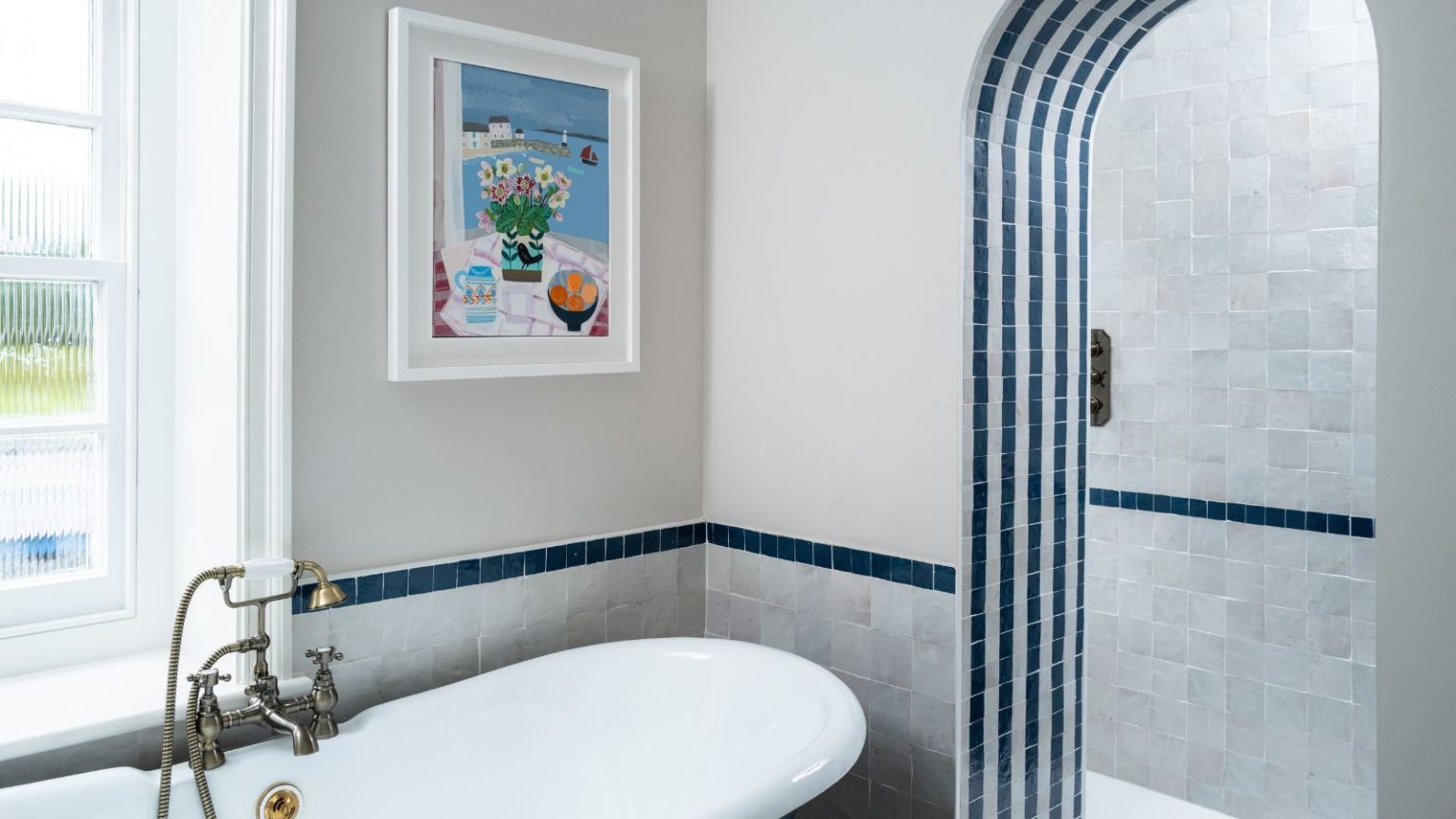 Je ne l’ai pas aimé pour nettoyer les vitres, mais un an plus tard, je ne jure que par cet ustensile de cuisine surprenant pour bannir facilement la moisissure dans ma douche A blue and white tiled bathroom with large bathtub with gold faucets, colorful artwork, and tiled archway to a shower behind