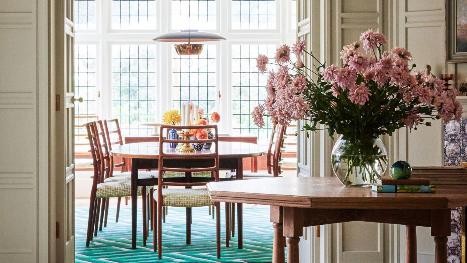3 zones de désordre cachées que les invités remarquent toujours immédiatement – Les pros révèlent comment les réparer avant l’hébergement de Noël A wooden dining table and chairs visible through an open doorway from an entryway. A large wooden table with pink flowers in a vase in the foreground.