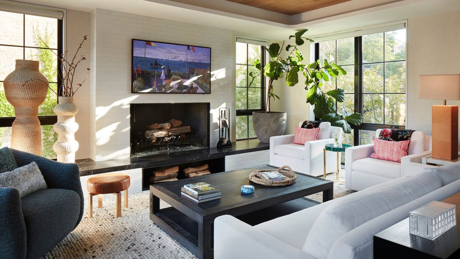 J’ai testé la barre de son 5 étoiles de Sonos, et elle a enfin un prix 5 étoiles avec 220 $ de réduction maintenant – juste à temps pour les films de Noël et les agréables soirées d’hiver Bright living room with white brick walls, paneled windows revealing outdoor area with trees, white sofas, dark coffee table, thick rug, black armchair, TV with seaside image, curved ornaments, and a large, potted plant.