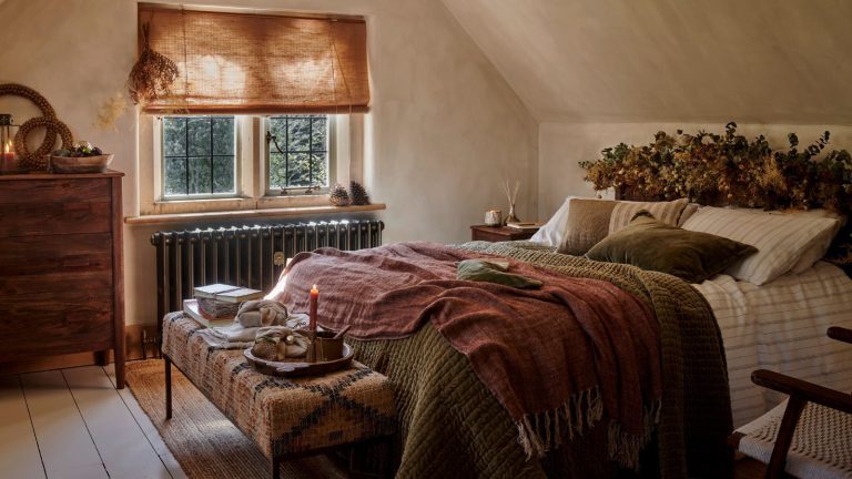 A limewashed attic bedroom with a bed made up with green and white bedding. A garland sits along the headboard.