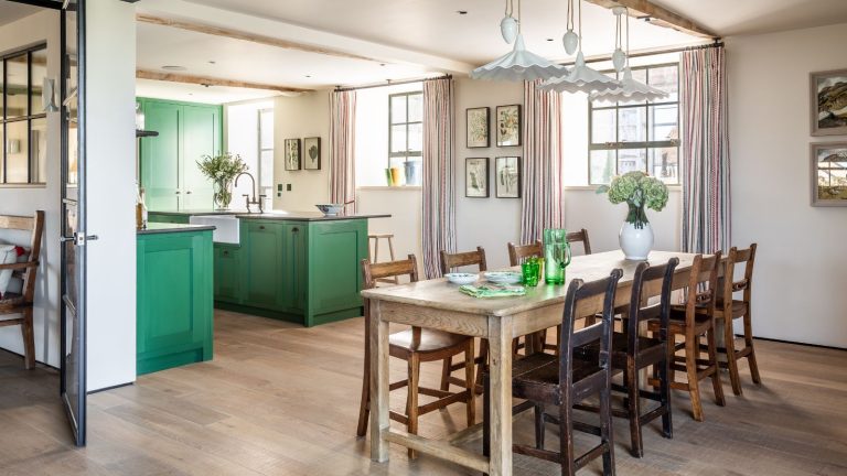Arrêtez de perdre du temps à essorer des vadrouilles qui sentent encore l’humidité : ce Dyson lave les sols en quelques secondes et à son prix le plus bas jamais vu Large kitchen and dining area with eight-seated wooden table and wooden chairs, hanging white lampshades, exposed wooden ceiling beams, green kitchen cabinets and a wooden floor. Small windows brightly light up the space.