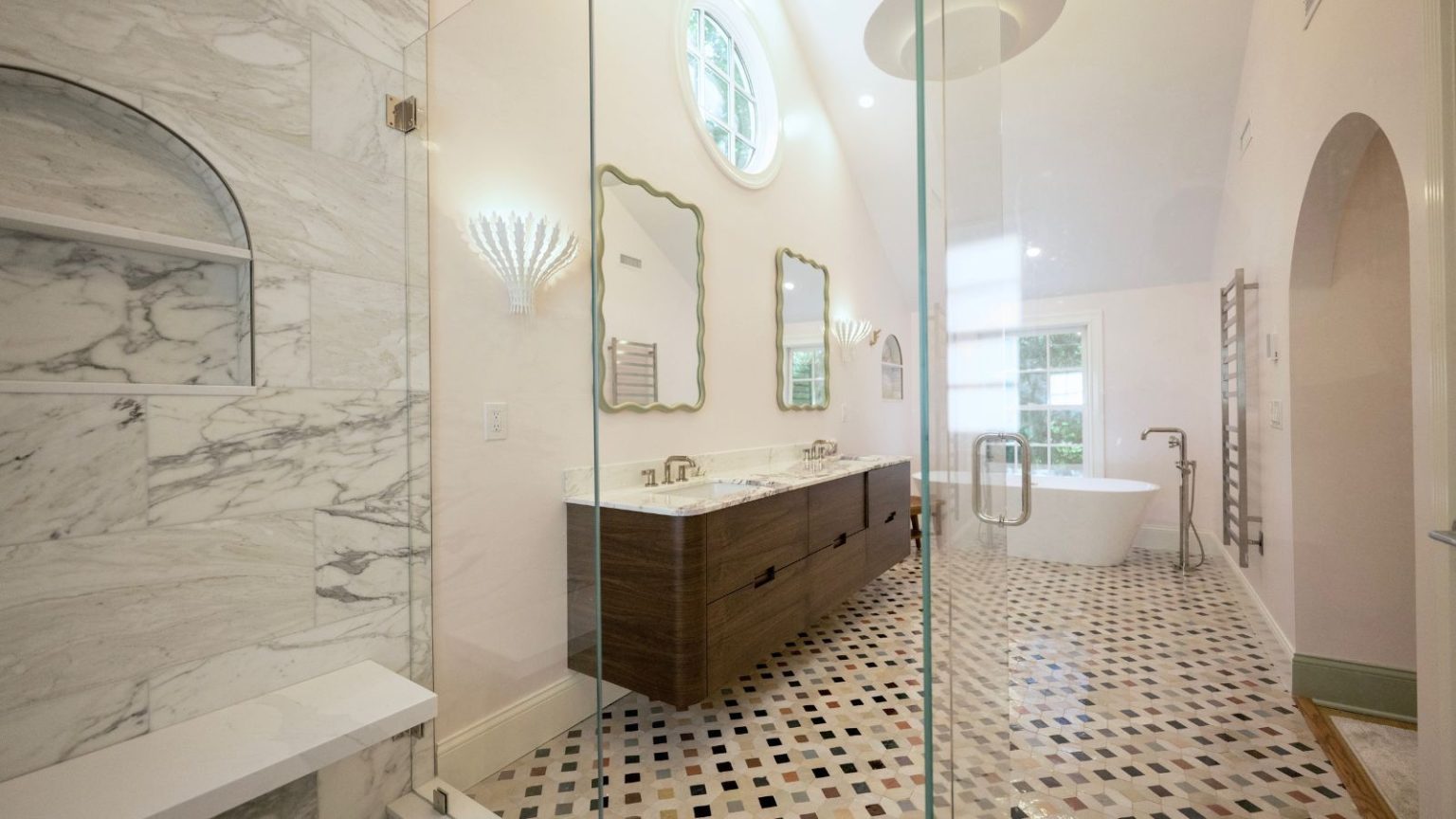 Un héros anti-moisissure à 16 $ avec 46 000 avis 5 étoiles – Les acheteurs ravis ne jurent que par ce spray sans gommage qui agit en quelques secondes A bright bathroom with a tiled floor, marble shower, wooden cabinetry, white countertops, and scalloped mirrors. In the far end of the bathroom is a white bathtub underneath a window.