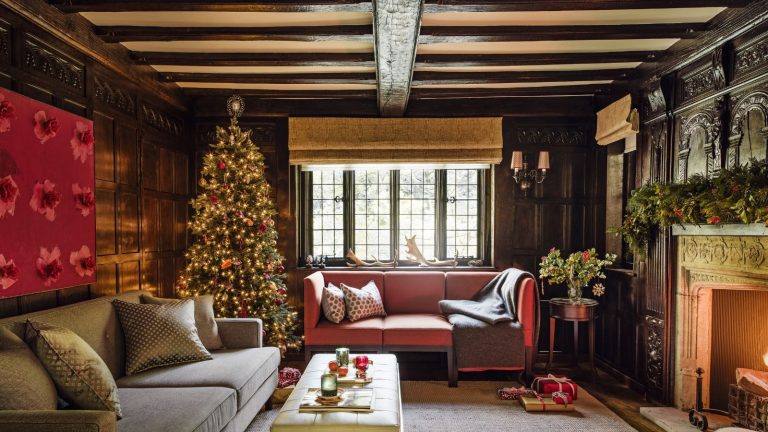 4 façons dont les lumières intelligentes peuvent rehausser les rassemblements de vacances en intérieur et économiser jusqu’à 90 % de votre consommation d’énergie habituelle A cosy living room with two sofas, with exposed ceiling beams, a tall decorated Christmas tree and fireplace with a lit fire.