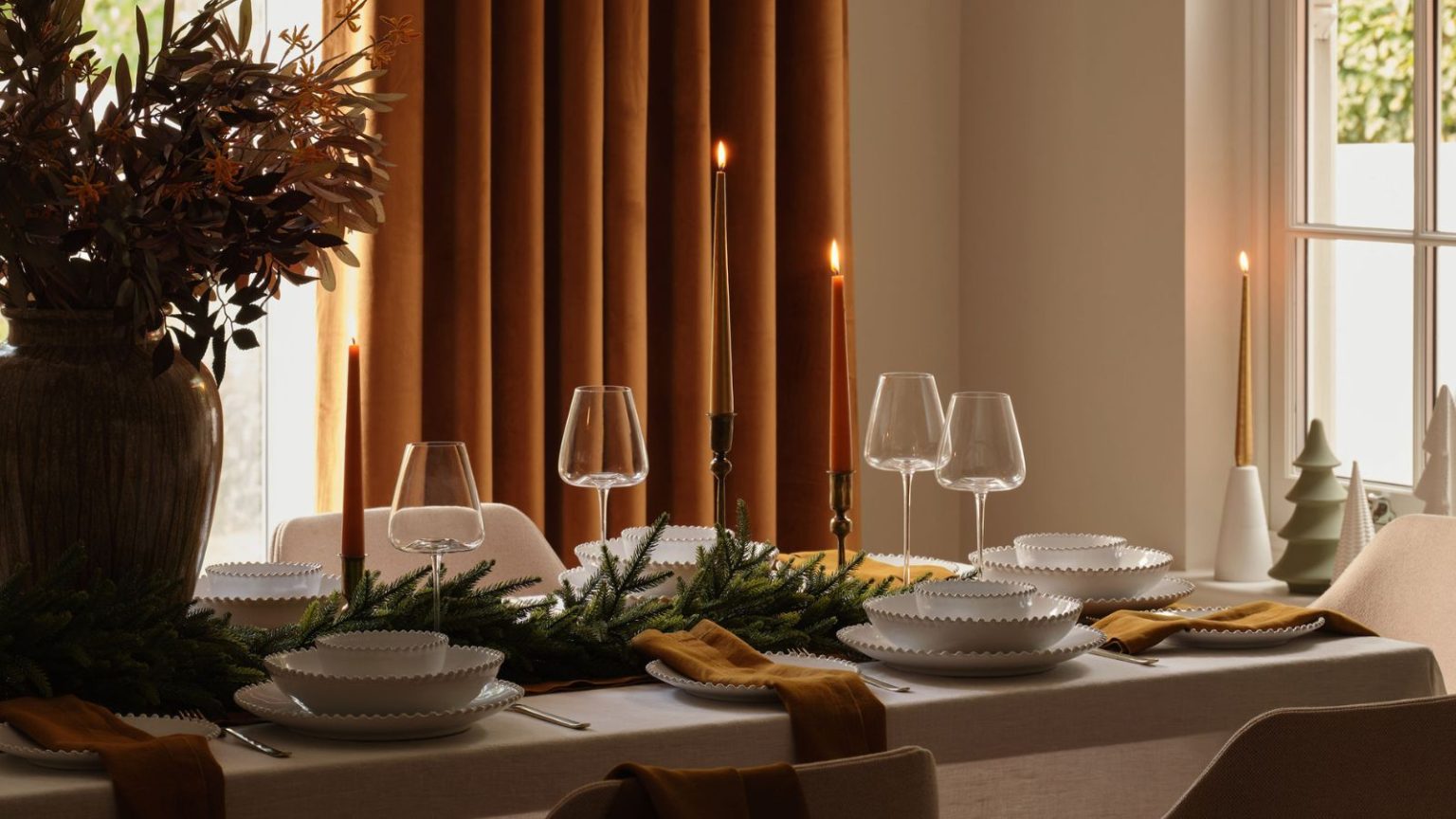 L’astuce des parfums de Noël que les professionnels du parfum utilisent pour masquer les odeurs de cuisine – C’est rapide, facile et rend également la maison confortable A dining table set with white bowels and decorated with a garland, candlesticks, and ceramic Christmas tree statues