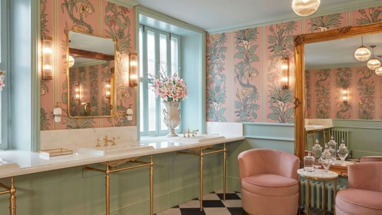 Augmentez le chauffage de votre radiateur avec cet article de salle de bain simple – cela ne prend que quelques secondes, mais vous devez éviter cette simple erreur Pastel green and peach bathroom with triple sinks and seating with Botanize Heritage Plaster Pink Wallpaper, which has vertical columns of pale green foliage on pink background