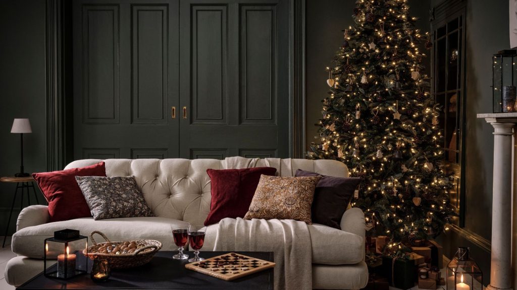 Les propriétaires sont invités à retirer cet article de Noël toxique – Les toxicologues préviennent qu’il peut compromettre votre santé A dark green color drenched living room with a white sofa with red velvet cushions, a well lit tree behind it