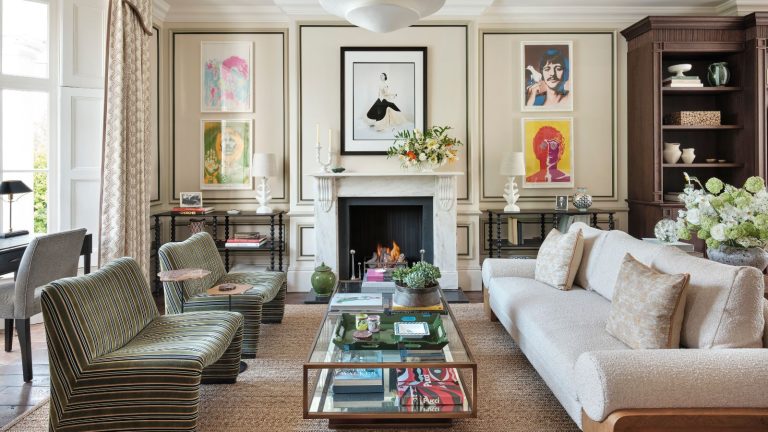 Répondez aux livraisons et dissuadez les intrus pendant que vous êtes absent avec la sonnette vidéo Arlo 2K à 59 $ à moitié prix Luxe cream living room with hardwood floors and rug with paneled walls and bookshelves. There is a cream teddy four-seater sofa, and two single striped green chairs around a brass and glass coffee table. Floor-to-ceiling cabinets are built in, along with full height curtains, giving it a luxe look