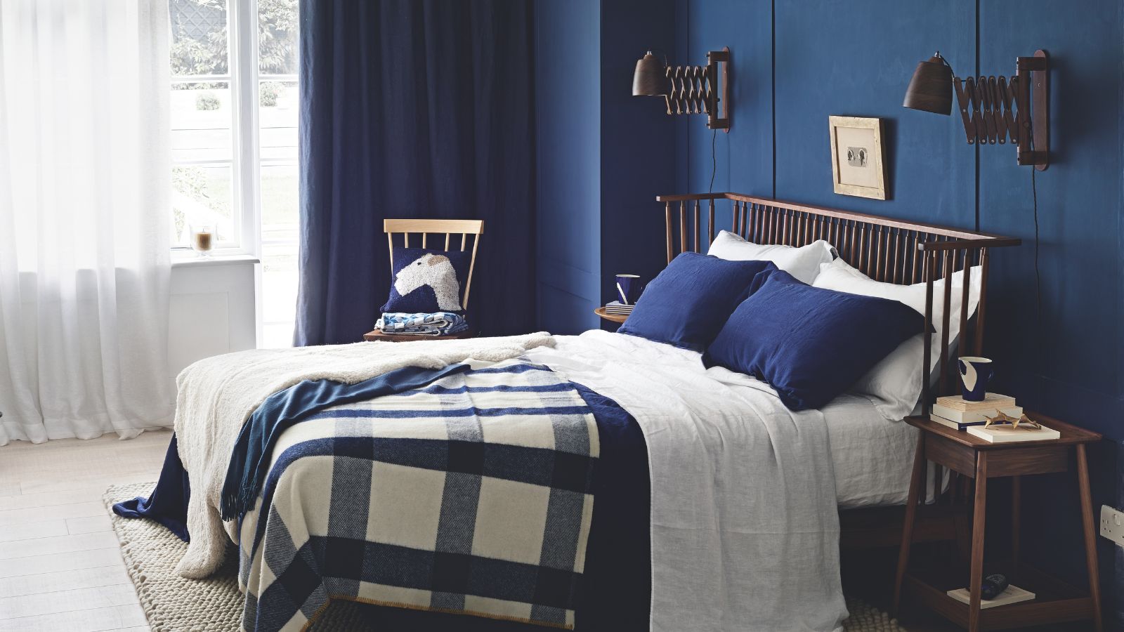 Une chambre bleue avec un grand lit double avec des oreillers bleus et un jeté bleu et blanc, ainsi que des rideaux blancs transparents au-dessus d'une grande fenêtre.