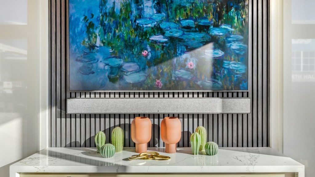 Votre barre de son ruine-t-elle l’esthétique de votre salon ? Voici comment le cacher comme un designer Soundbar and TV showing watercolor art mounted on paneled wall, above marble surface with artificial cacti and pots.