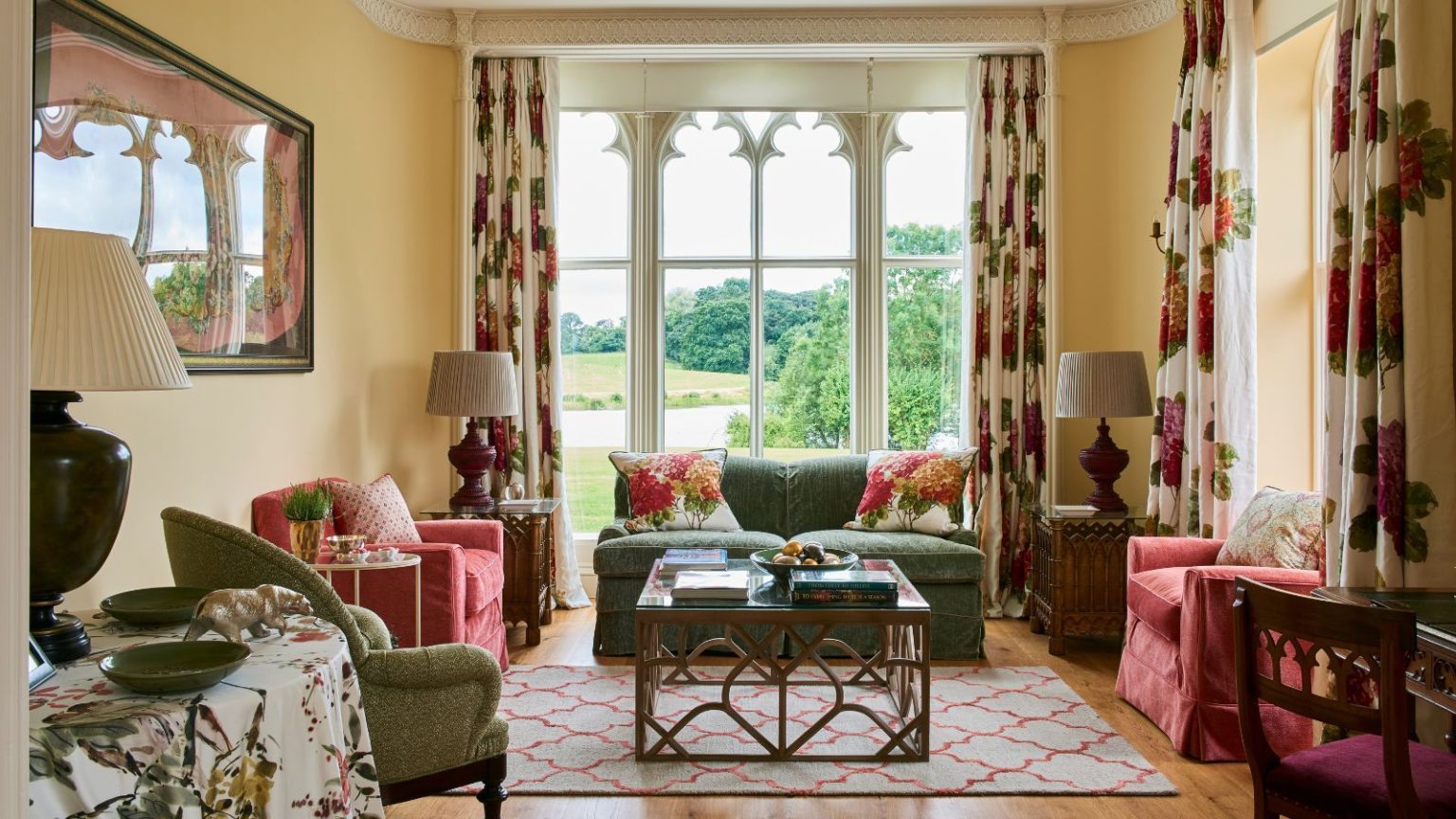 Nous avons testé 90 aspirateurs et le PowerDetect sans fil Shark à vidage automatique est le meilleur moyen d’arrêter de toucher la poussière (maintenant 120 $ moins cher) Living room with wooden floor and gothic window with views to the garden. Red and green upholstered chairs and sofa and floral curtains and cushions.