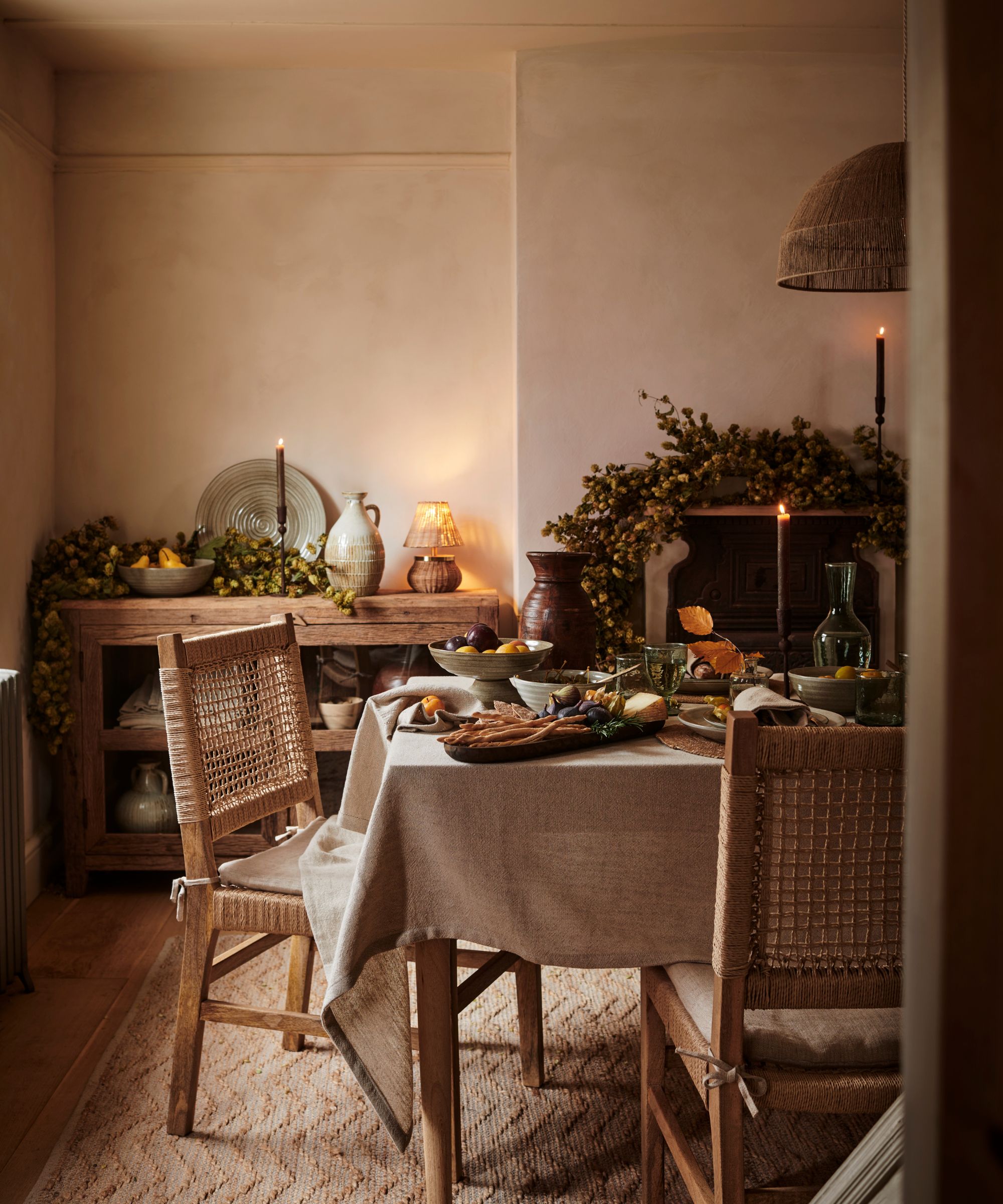 Une salle à manger neutre décorée pour l'automne, avec des guirlandes drapées sur le manteau et le buffet.