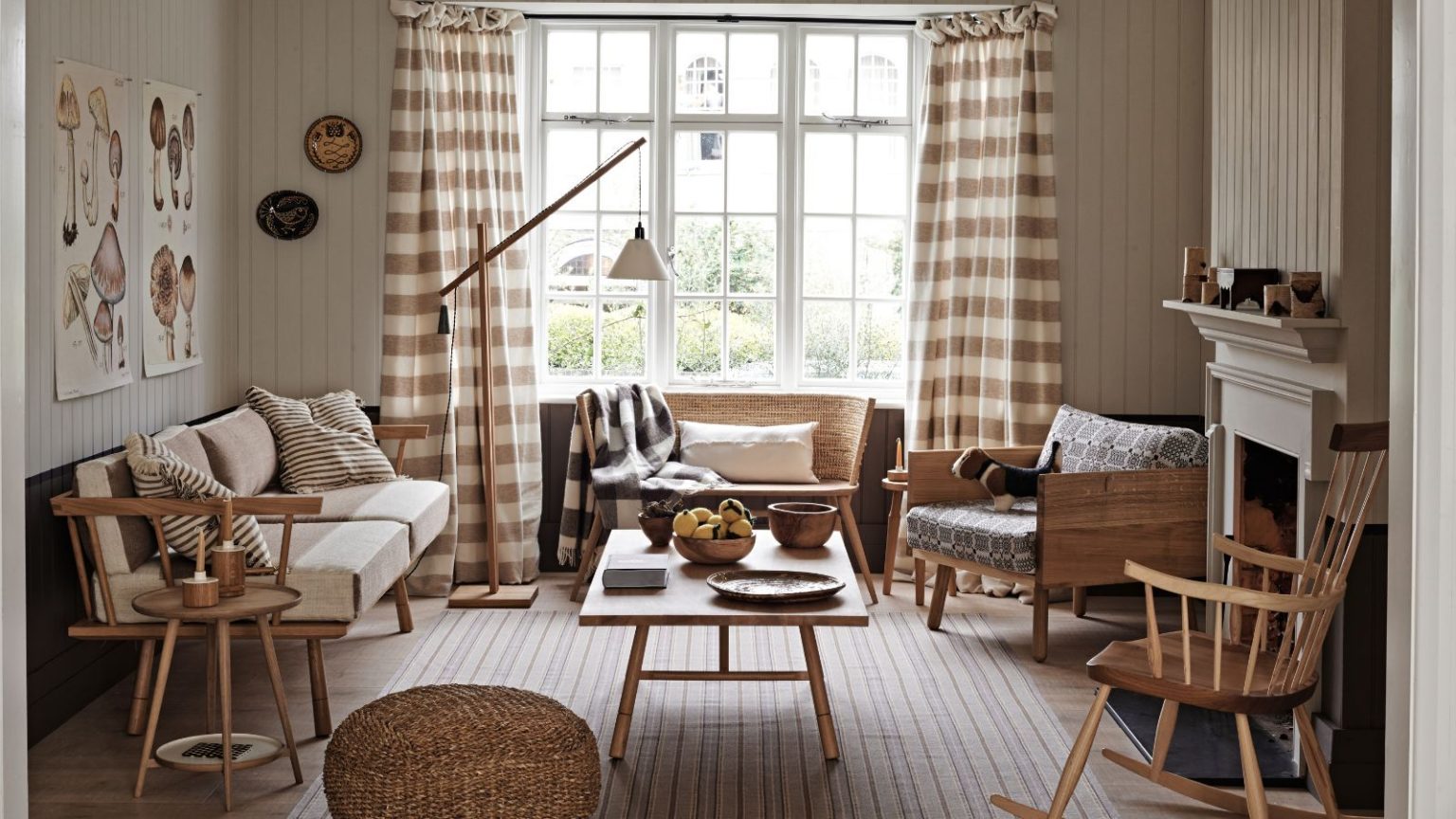 Un designer m’a dit une astuce de rideau rapide et chic qui arrête instantanément les courants d’air – et cela ne gâchera pas votre décor A neutral living room with wall panelling, a striped rug, wooden table, wooden chair, brown and white gingham curtains over a large window, and a white mantelpiece.