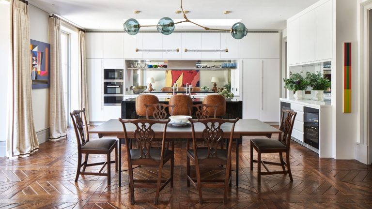 Kitchen diner with wooden flooring, white fitted kitchen cupboards, large kitchen table and carved wooden chairs. A redesigned and renovated London townhouse, home of Mikael Lofberg and his partner.