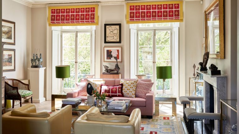 Arrêt! Ne recyclez pas cet article ménager courant : utilisez-le pour bannir facilement et gratuitement les poissons d’argent, révèlent les experts. Bright, multi-colored living room with two large windows, a pin sofa, two leather armchairs, a coffee table with flowers and books, a patterned rug, and miscellaneous lights and framed pictures.