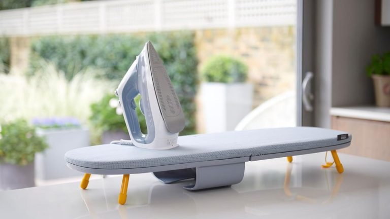 The Joseph Joseph tabletop folding ironing board, out on a white counter, with an iron on top