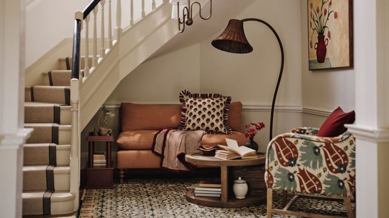 A cozy seating area with a small sofa and an arm chair nestled under a curling stair case. A large sculptural lamp beside them and a low hanging pendant.